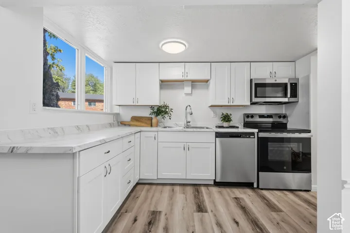 Kitchen featuring white cabinetry, light-toned countertops, stainless steel appliances, and wood-finish flooring
