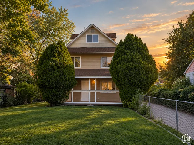 Three-story structure with horizontal siding, a covered front porch, and a fenced side path