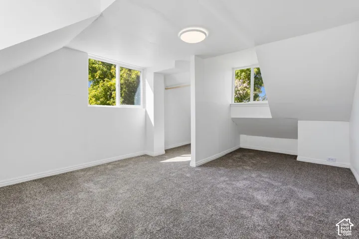Attic room with sloped ceilings, two windows, gray carpet, and a built-in closet with a hanging rod