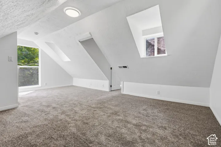 Sloped ceilings with multiple windows, recessed lighting, and neutral carpeting