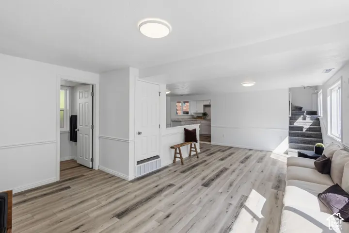 Spacious open-concept living area featuring wood-finish flooring, white walls with wainscoting, and recessed lighting