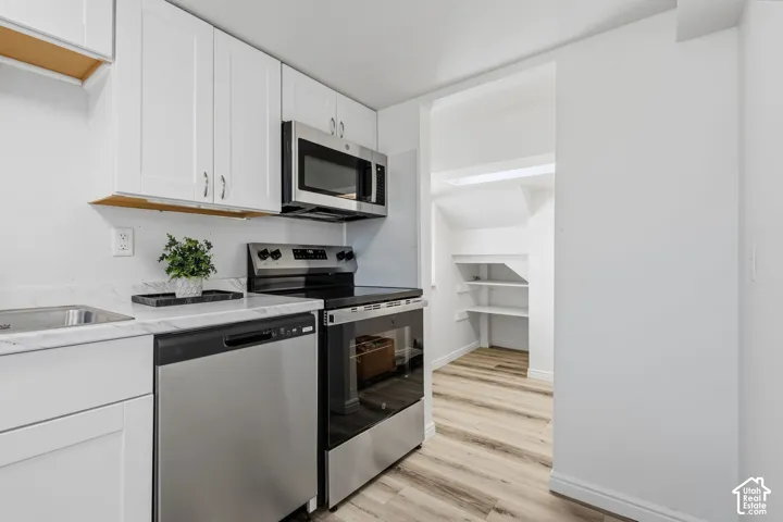 Kitchen featuring white cabinetry, stainless steel appliances, a single basin sink, and light-toned wood-finish flooring