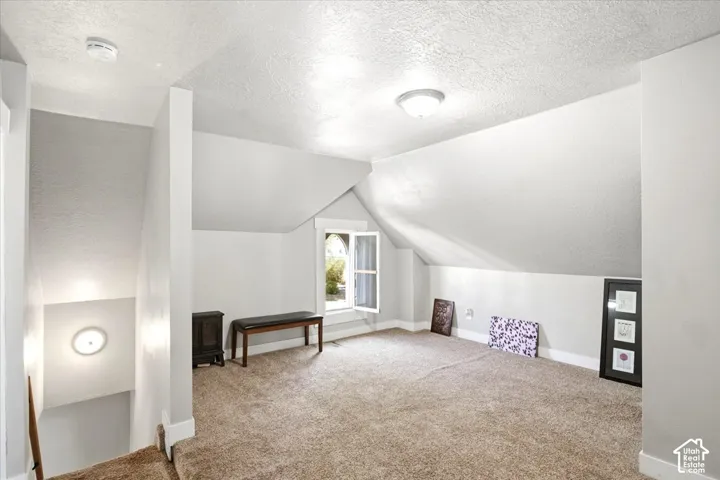 Carpeted loft area with sloped ceilings, a window, and flush-mount lighting fixtures