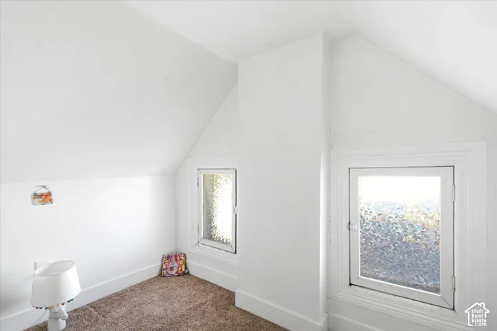 Attic space with sloped ceilings, two distinct window openings, and wall-to-wall carpeting