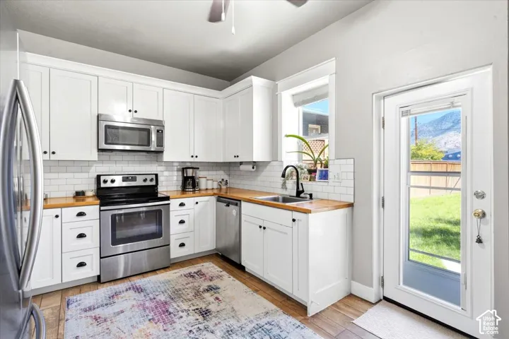 Kitchen featuring white shaker cabinetry, stainless steel appliances, wood-finish countertops, subway tile backsplash, and a full-light exterior door