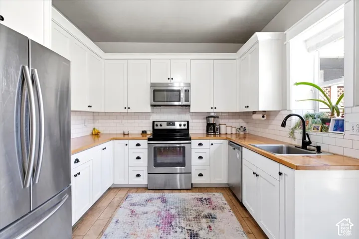 U-shaped kitchen featuring white cabinetry, wood-finish countertops, subway tile backsplash, stainless steel appliances, and wood-finish flooring