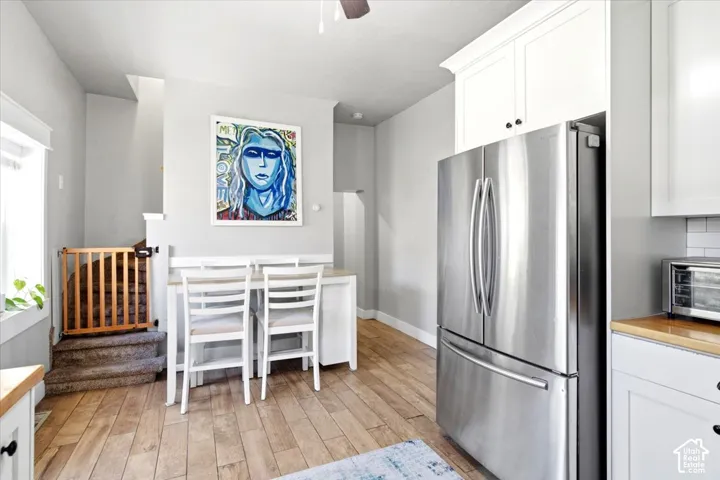 Stainless steel French door refrigerator, white upper and lower cabinetry, wood-finish flooring, light-toned countertops, and a white subway tile backsplash