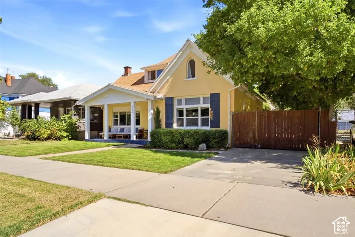Yellow exterior with white trim, covered front porch, dormer window, and mature front landscaping