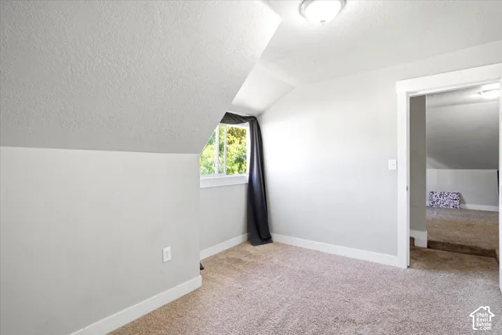 Carpeted room with sloped ceiling, window, and flush mount lighting