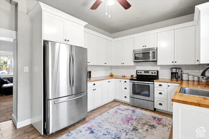 White cabinetry with black hardware, wood-finish countertops, stainless steel appliances, and subway tile backsplash