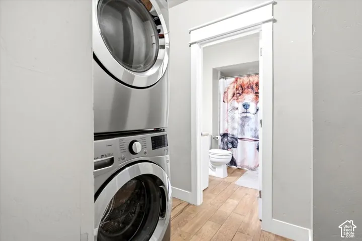 Stacked washer and dryer unit, wood-finish flooring, white trim, white door, and white toilet