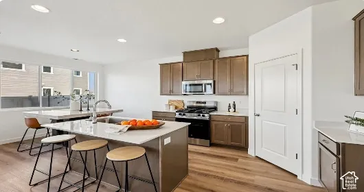Kitchen featuring wood-finish flooring, recessed lighting, white countertops, stainless steel appliances, and brown cabinetry. This home is under construction. Pictures are of a similar home.