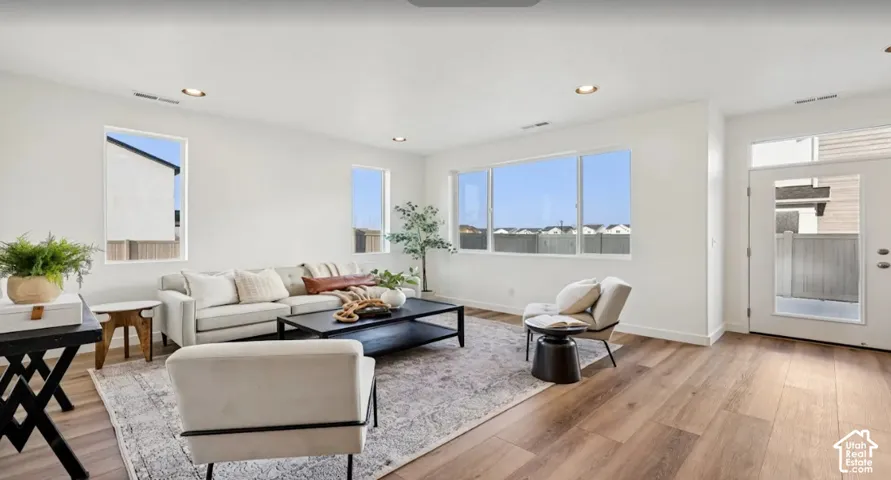 Spacious living area featuring large windows, wood-finish flooring, recessed lighting, and a white paneled door with transom window. This home is under construction. Pictures are of a similar home.