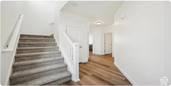 Carpeted staircase with white balusters, wood-finish flooring, and white walls. This home is under construction. Pictures are of a similar home.