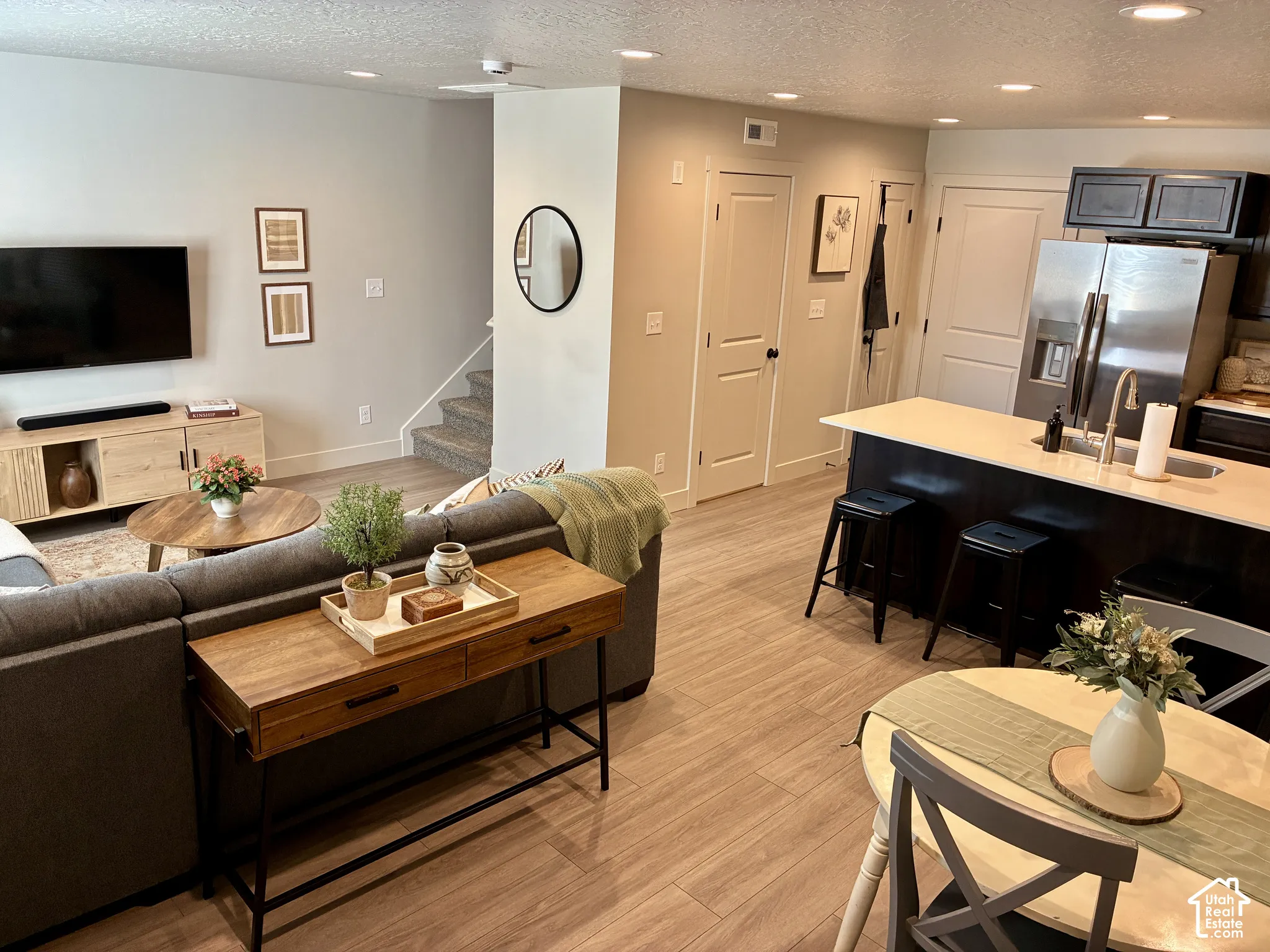 Open-concept living space featuring wood-finish flooring, recessed lighting, a kitchen island with seating, and stainless steel appliances. Couch, TV, TV stand, kitchen table and chairs included*