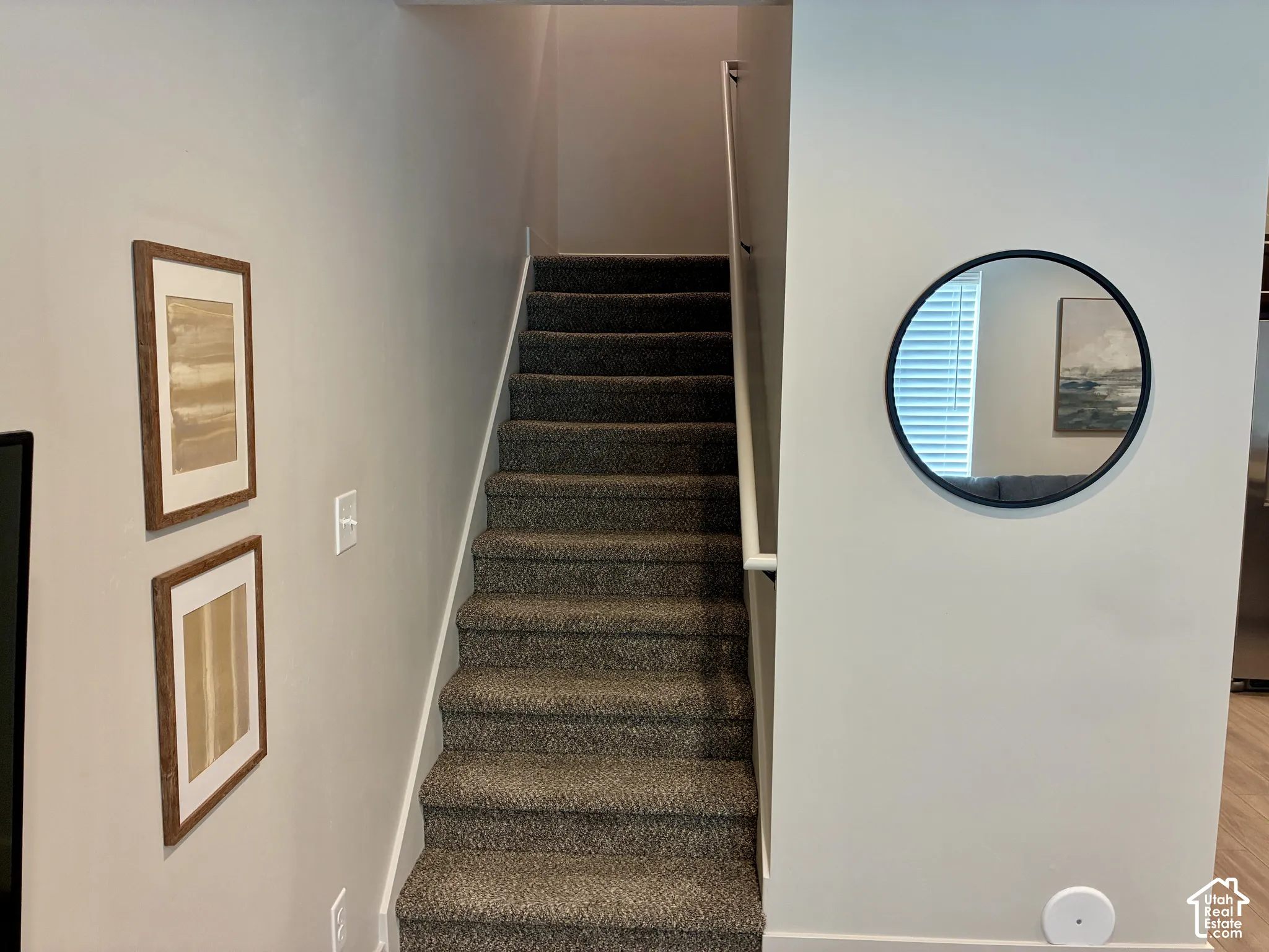 Carpeted stairway with a white handrail, complemented by light-colored wall paint