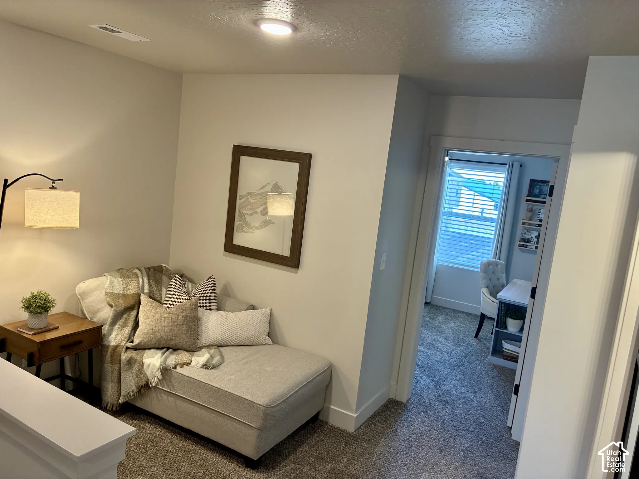 Carpeted hallway with a built-in recessed light, white trim, and a doorway opening to an additional room