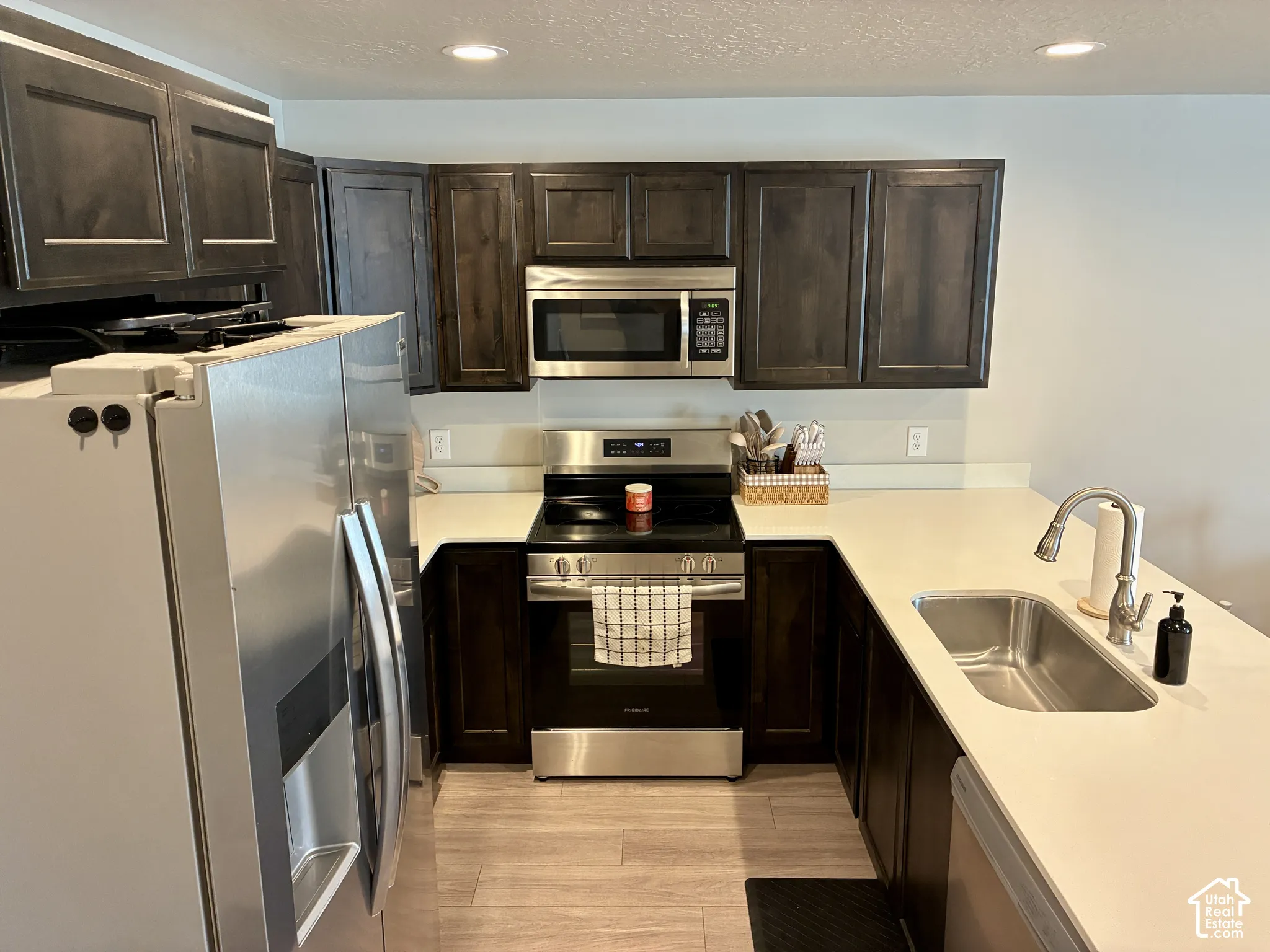 Dark wood-finish cabinetry, stainless steel appliances, light-toned countertops, and recessed lighting