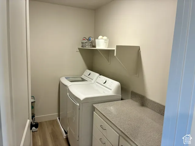 Laundry area featuring wood-finish LVP flooring, white cabinetry, integrated shelving, and a speckled countertop. Located on second floor with bedrooms. Custom folding counter and cabinets added by seller. Washer and dryer included!