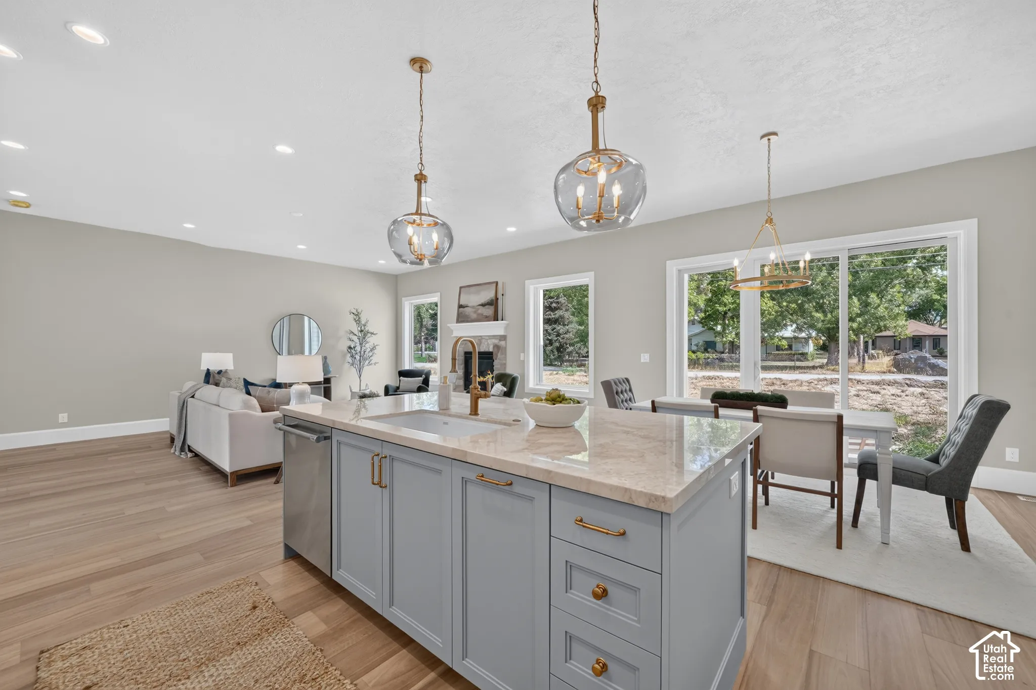 Expansive open-concept design featuring wood-finish flooring, a kitchen island with stone countertop, and a fireplace with a stone surround
