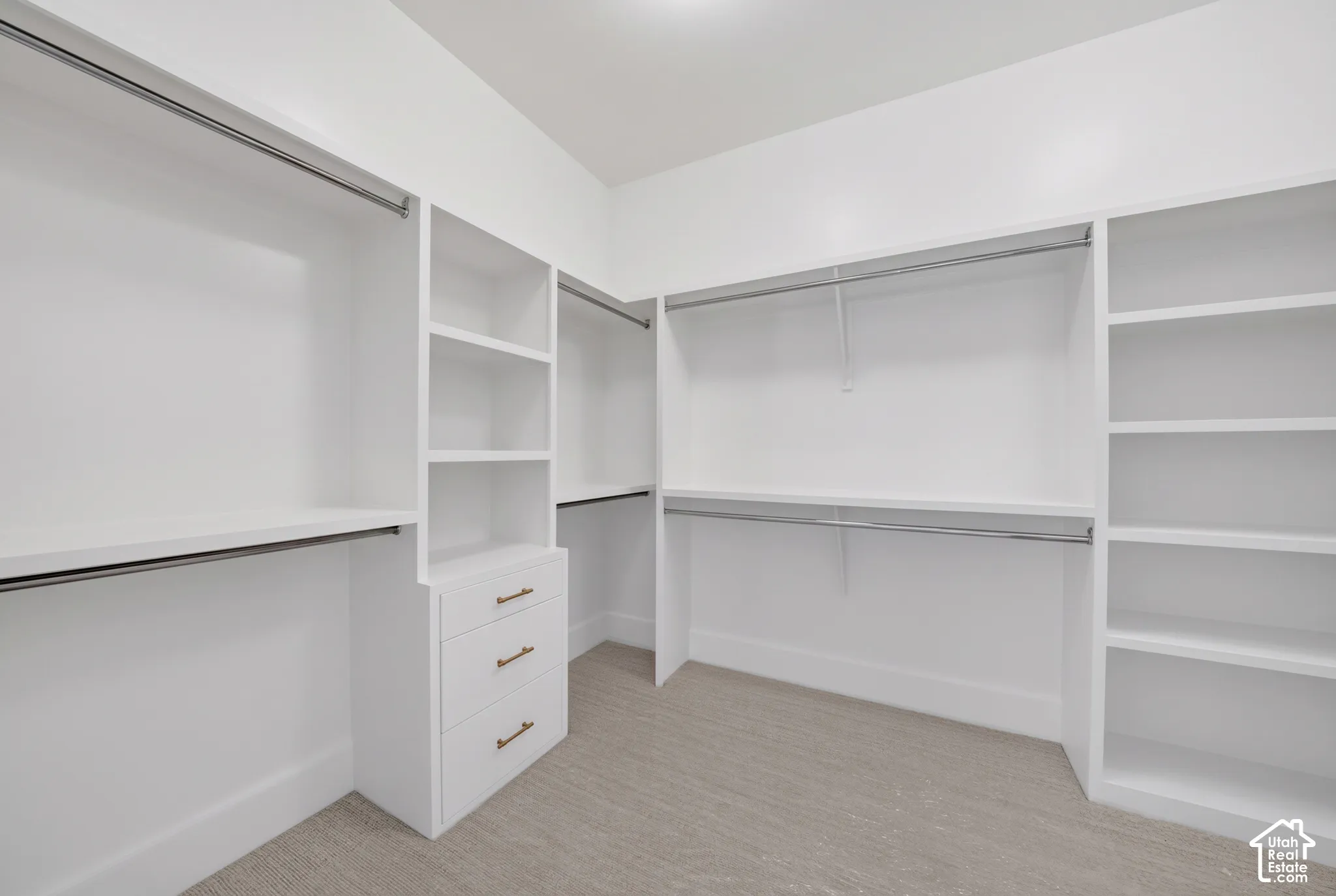 Integrated custom closet system with white cabinetry, multiple hanging rods, built-in shelving, and drawers with brass hardware