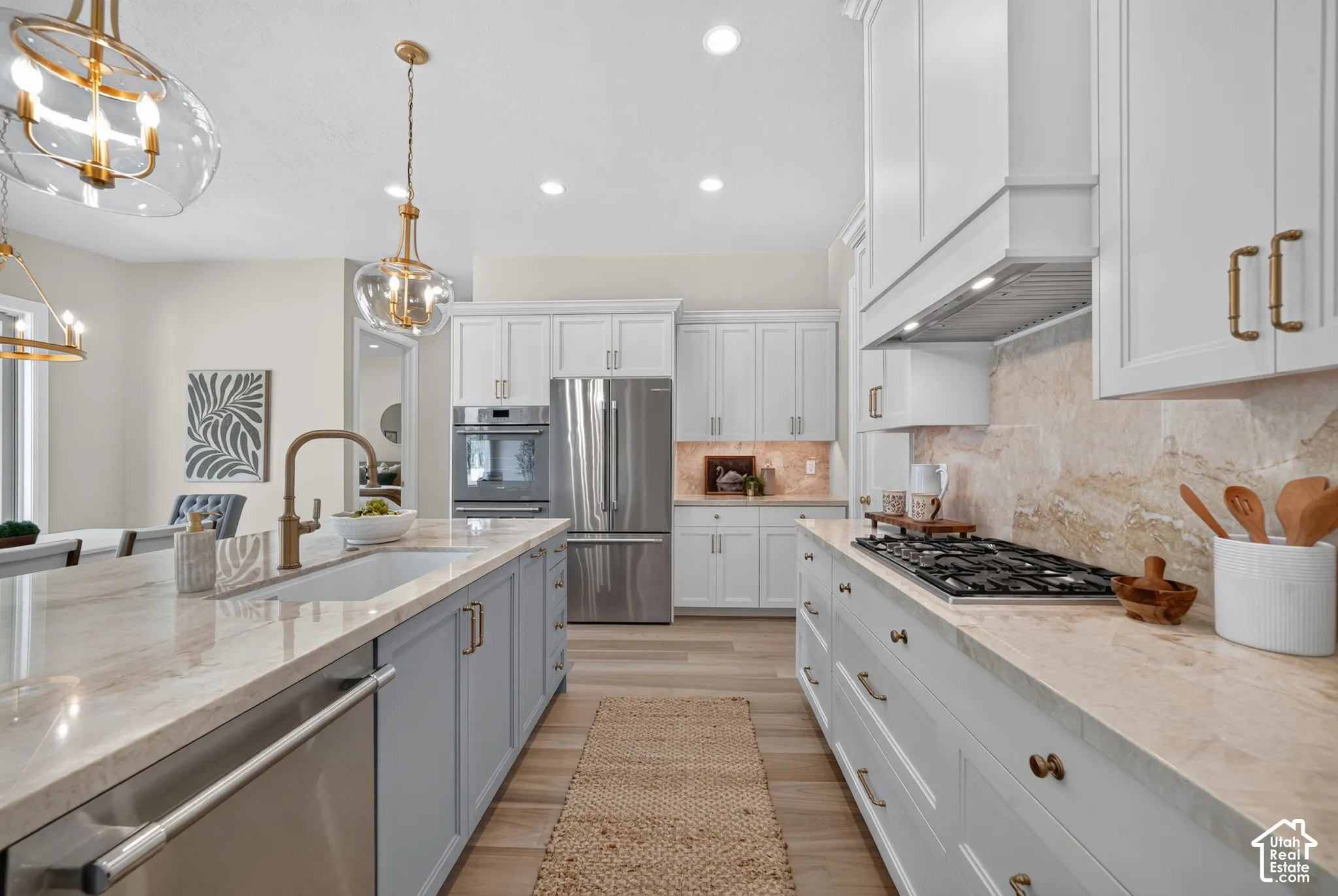 Kitchen featuring light cabinetry, a large central island with a sink, stainless steel appliances, a gas range with a range hood, and light-toned countertops
