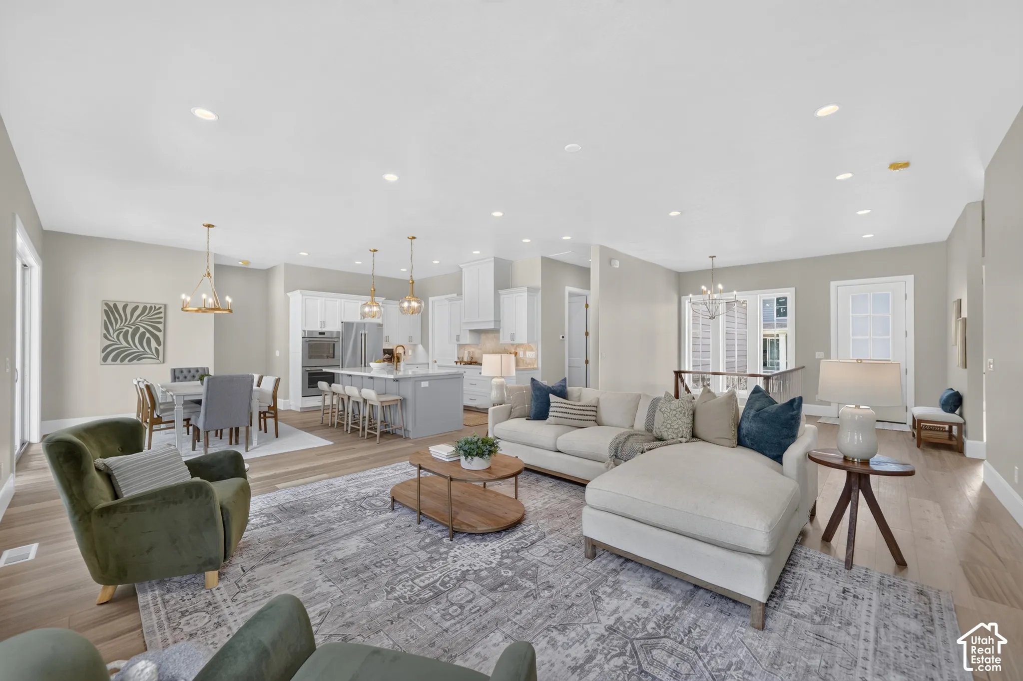 Recessed lighting throughout, wood-finish flooring, white kitchen cabinetry, stainless steel appliances, and a kitchen island with bar seating