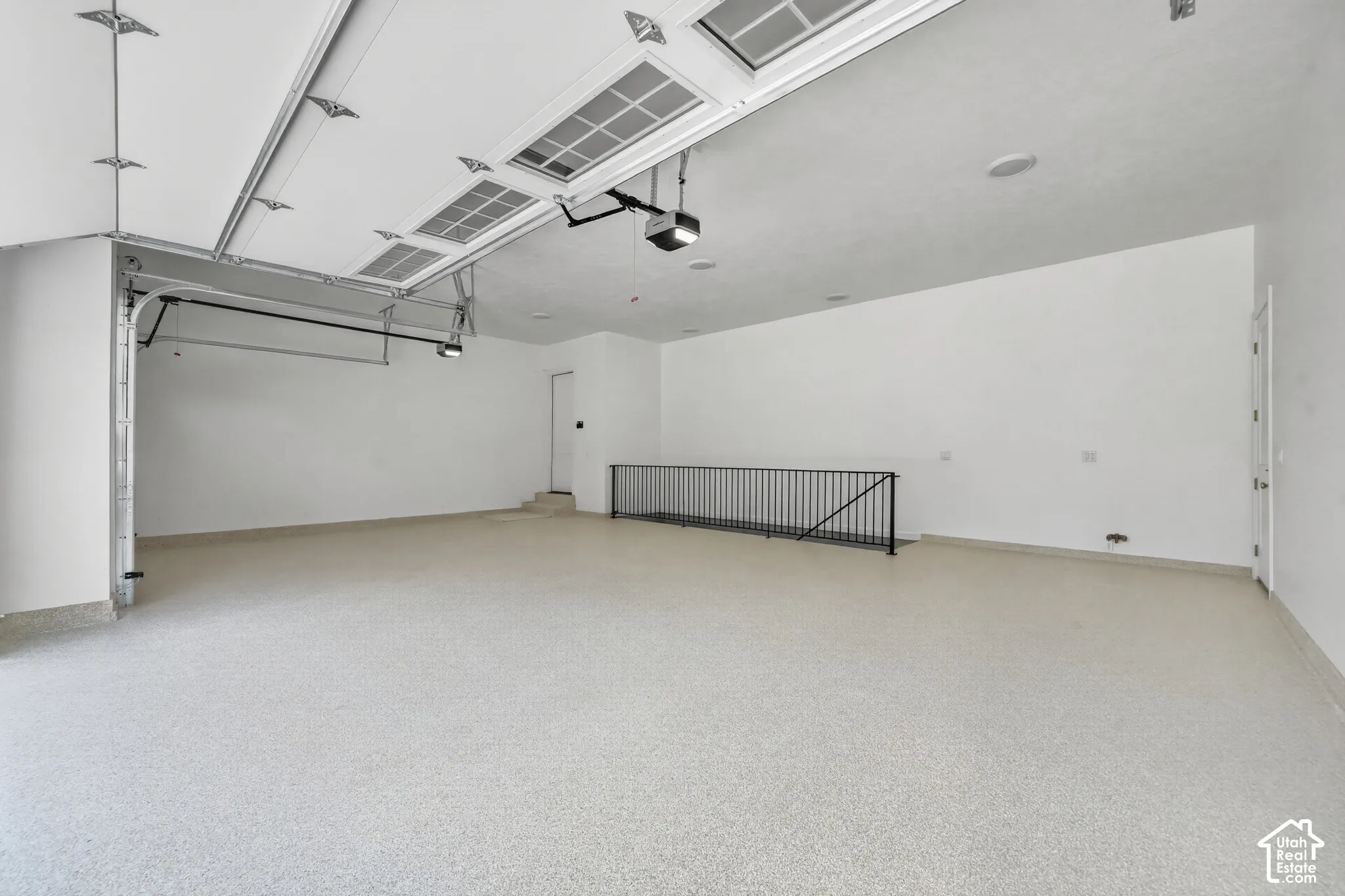Spacious garage with light-toned epoxy flooring, automatic garage door opener, and a built-in railing