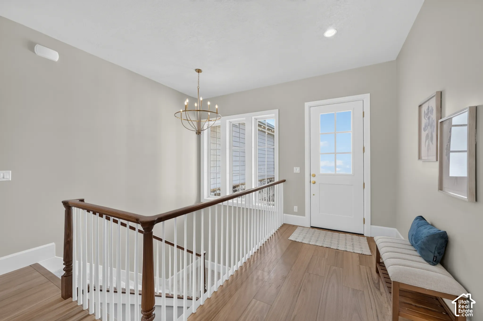 Hardwood-finish flooring, white spindle staircase with wood handrail, windowed exterior door, multiple casement windows, and a bronze chandelier