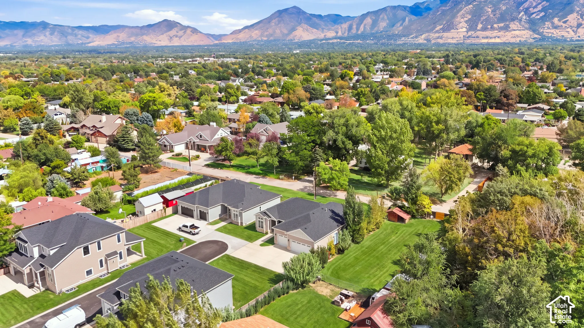 Lush landscaping with mature trees, expansive green spaces, mountain backdrop, and varied residential architecture