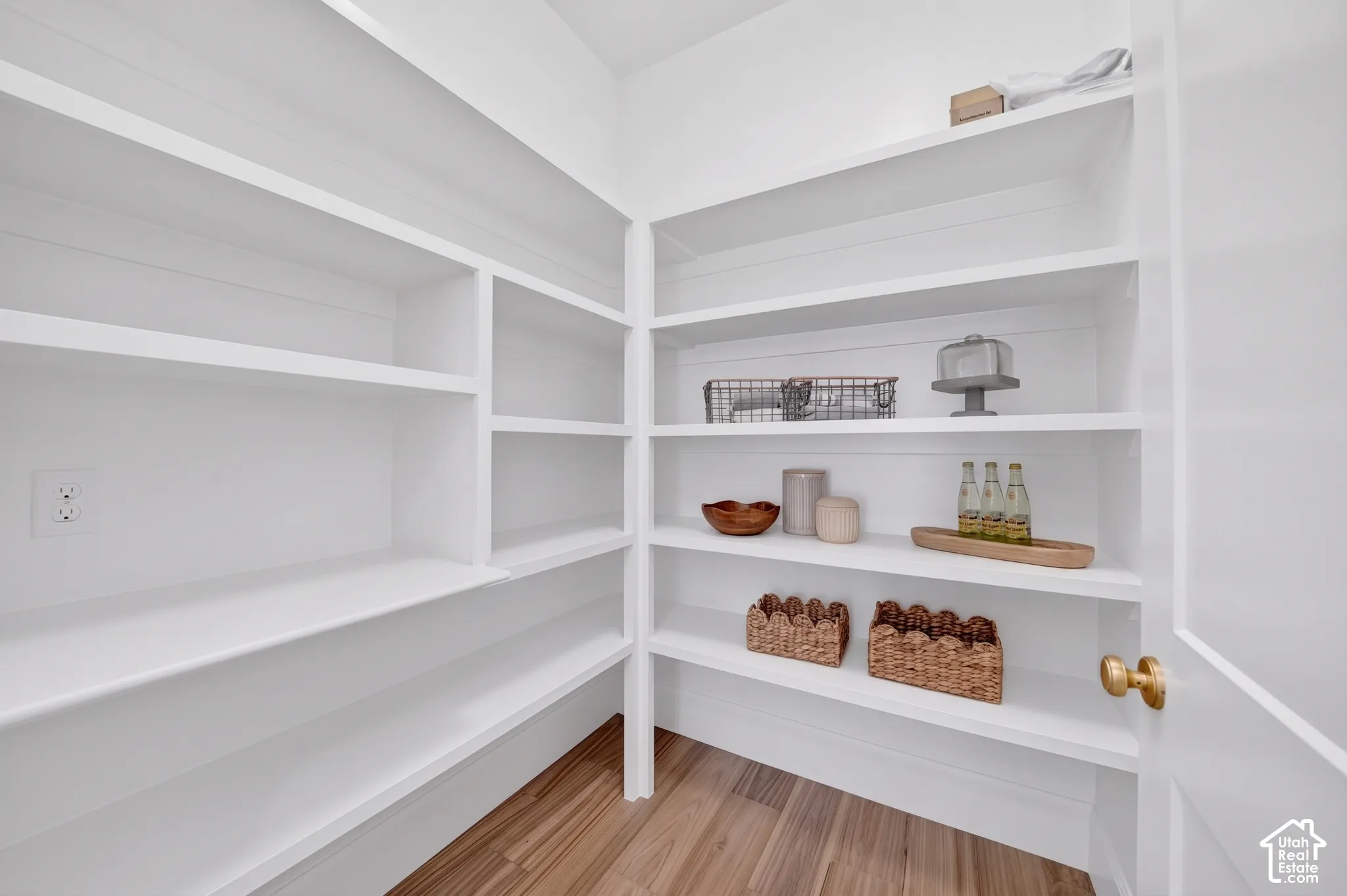 Corner pantry featuring built-in shelving, wood-finish flooring, and a brass door handle