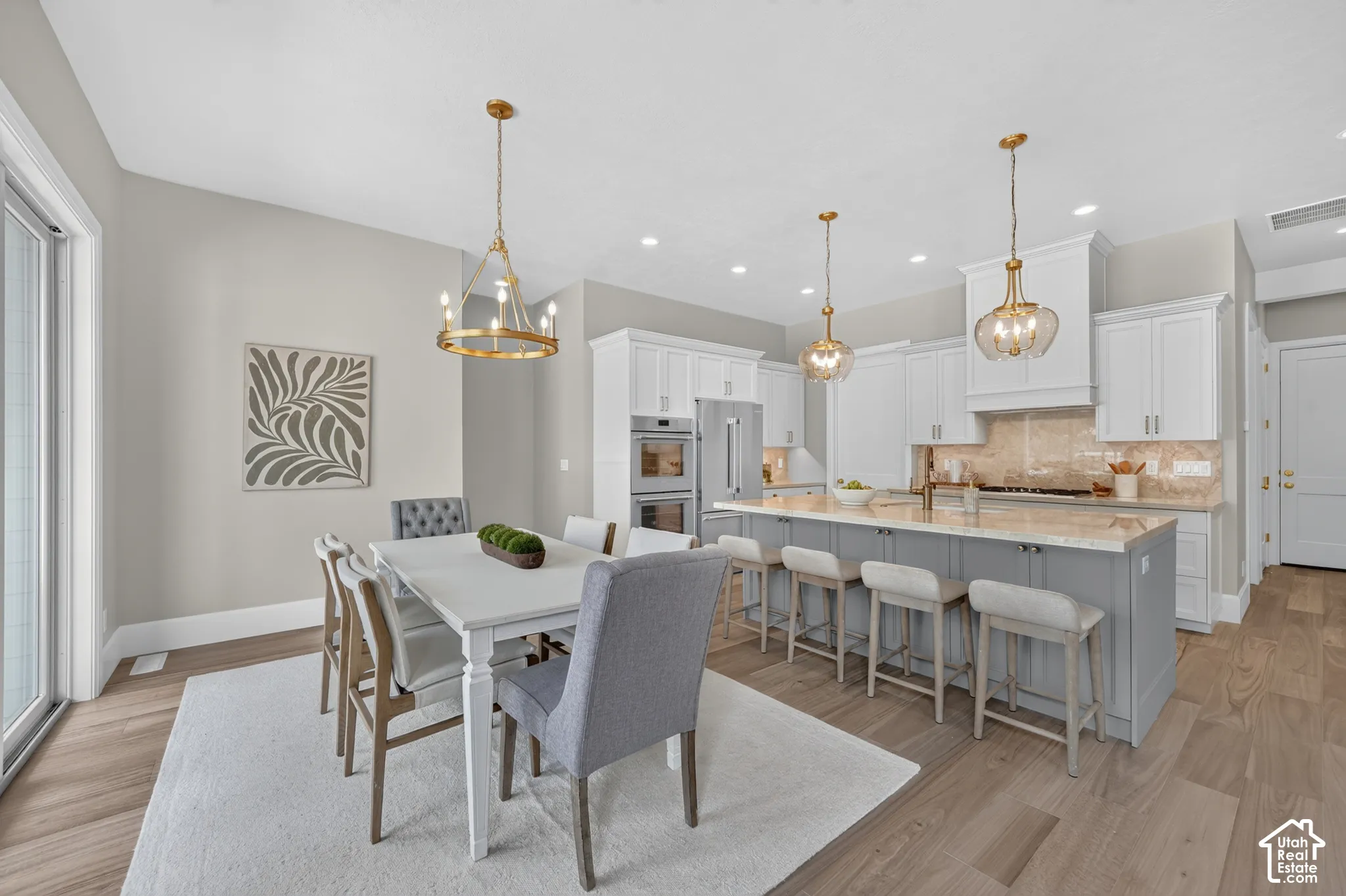 Open-concept kitchen and dining area featuring light wood-finish flooring, a kitchen island with seating, pendant lighting, and white cabinetry