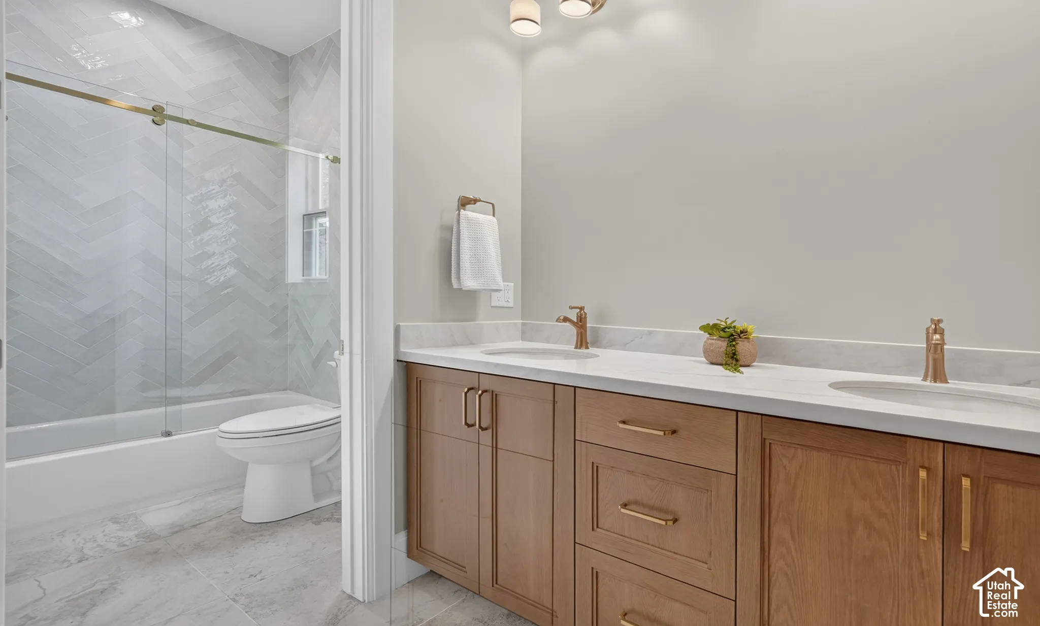 Dual vanity with light wood-finish cabinetry, white countertop, and gold-toned fixtures