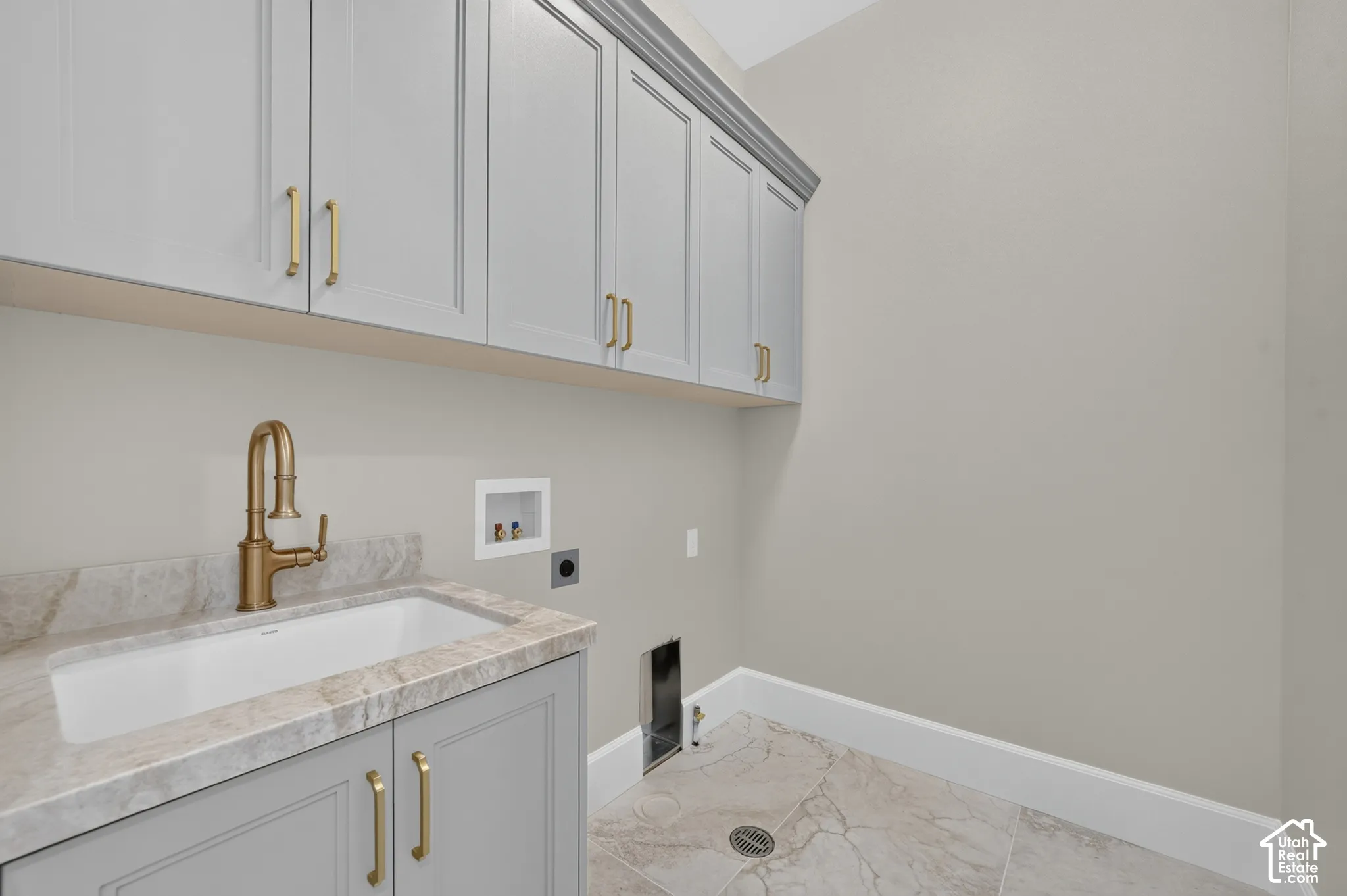 Wall-mounted cabinetry, integrated sink with a bronze-finish faucet, stone countertop, and large format floor tile