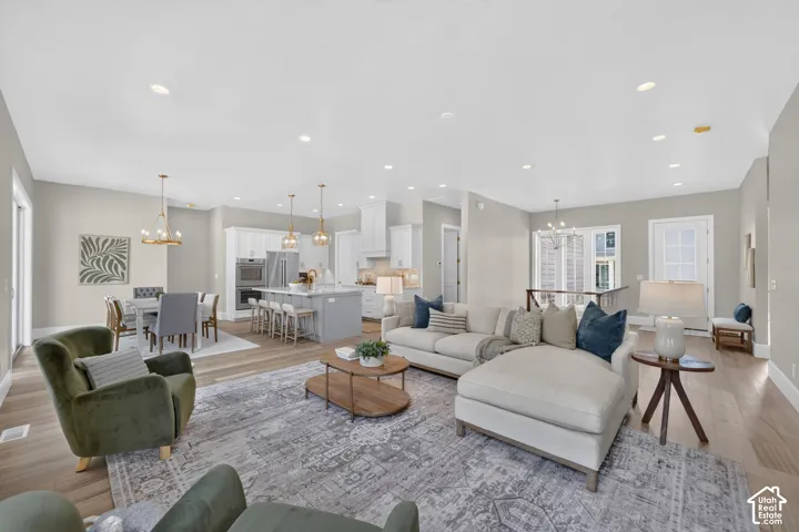 Recessed lighting throughout, wood-finish flooring, white kitchen cabinetry, stainless steel appliances, and a kitchen island with bar seating