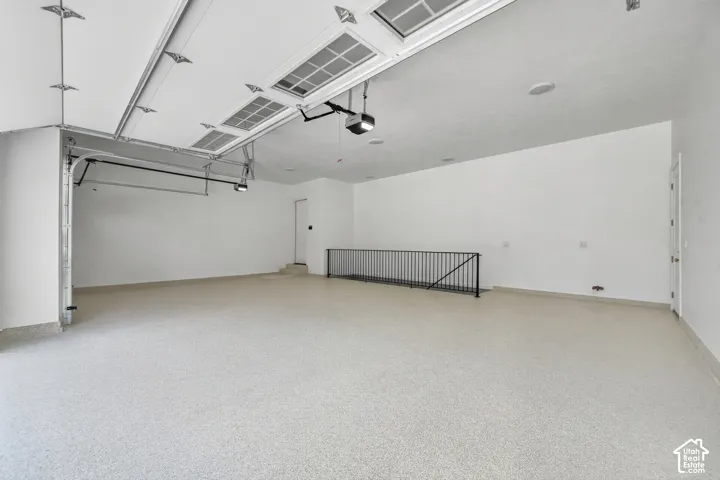 Spacious garage with light-toned epoxy flooring, automatic garage door opener, and a built-in railing