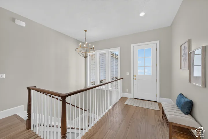 Hardwood-finish flooring, white spindle staircase with wood handrail, windowed exterior door, multiple casement windows, and a bronze chandelier