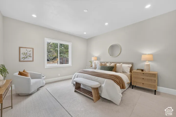 Recessed lighting illuminates the room, featuring a large window with white trim, light-toned carpeting, and light-colored walls