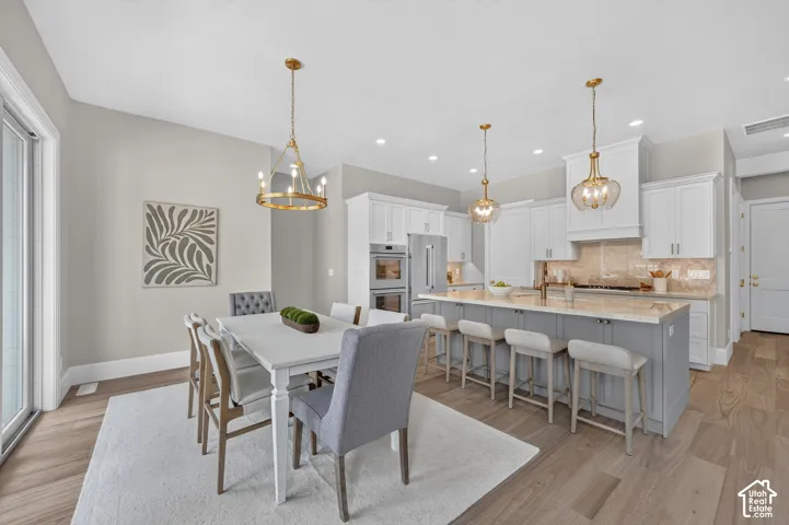 Open-concept kitchen and dining area featuring light wood-finish flooring, a kitchen island with seating, pendant lighting, and white cabinetry