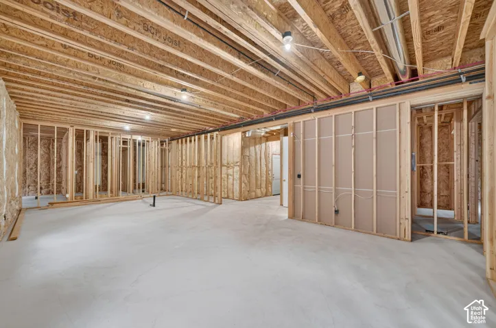Unfinished basement with exposed wood joists and framed walls, featuring a concrete floor