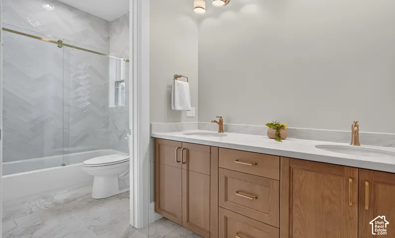 Dual vanity with light wood-finish cabinetry, white countertop, and gold-toned fixtures