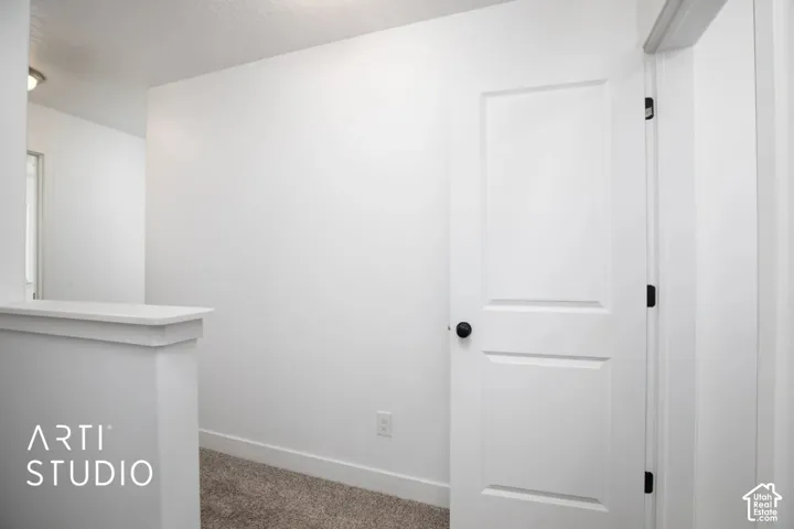 White interior door with a black knob and hinges, accompanied by a half-wall partition, and carpeted flooring
