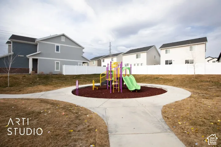 Community playground with a colorful play structure, surrounded by a concrete pathway and wood chip surfacing