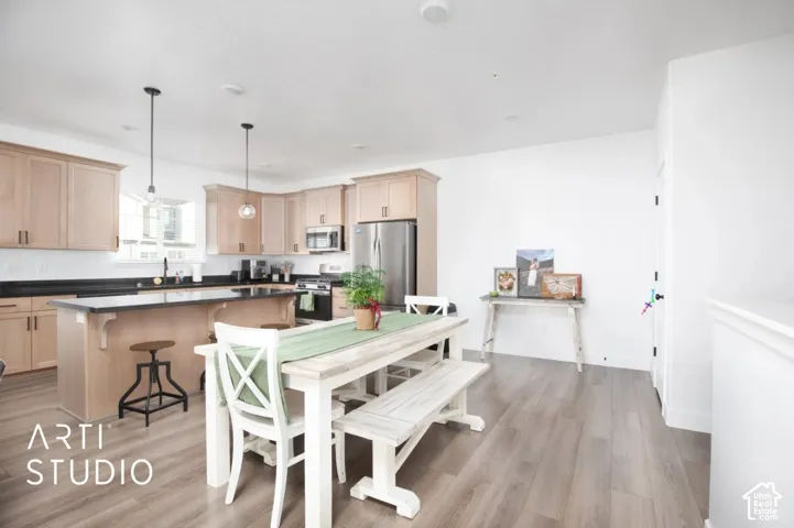 Kitchen featuring light wood-finish cabinetry, dark countertops, stainless steel appliances, and two pendant light fixtures