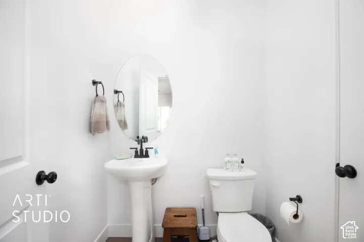 White pedestal sink with a matte black faucet, oval mirror, and white walls