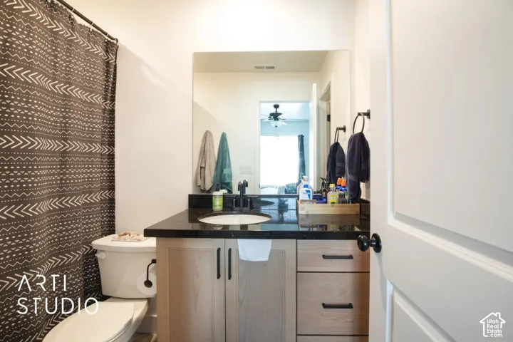 Vanity with a vessel sink, dark countertop, and light wood-finish cabinetry featuring matte black hardware
