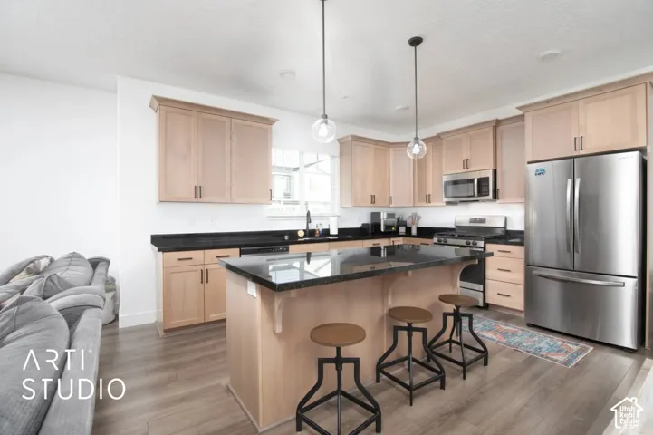 Kitchen featuring a central island with seating, stainless steel appliances, black countertops, and wood-finish flooring