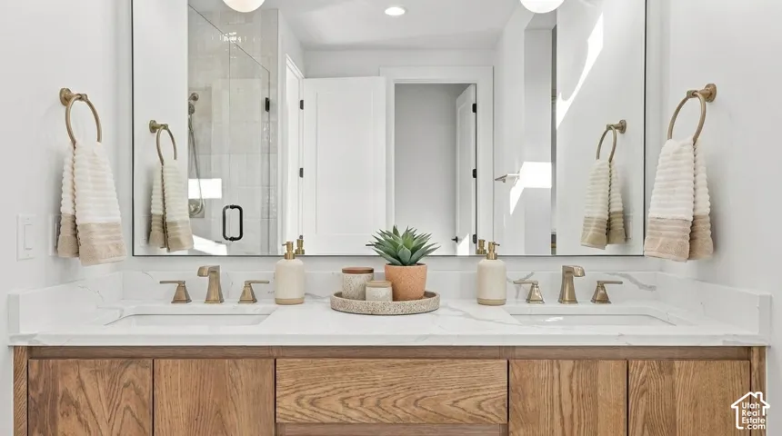 Dual vanity with wood-finish cabinetry, white countertop, rectangular undermount sinks, and brass-finish fixtures