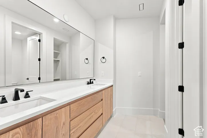 Dual undermount sinks with matte black fixtures, an expansive vanity mirror, wood-finish cabinetry, and light-toned floor tiling