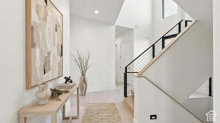 Dual-height foyer with a contemporary staircase featuring a light wood handrail and black metal balusters, illuminated by recessed lighting and natural light from tall windows